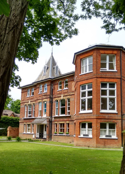 Victorian brick house with white trim and garden setting under green trees.