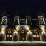 Victorian brick building facade at night with illuminated arched entrances and festive wreaths.