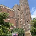 Tall, historic brick and stone building with a prominent tower under a blue sky.