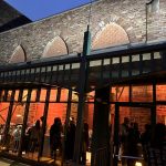 Historic brick building facade with arched windows and modern glass entrance at dusk.