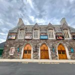 Stone theater building with multiple gables under a cloudy sky.