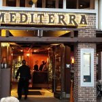 Exterior view of a restaurant named "MEDITERRANEA" with warm interior lighting visible.
