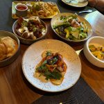 Assortment of dishes on a wooden table at a restaurant, including appetizers and main courses.