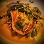 Seared salmon fillet with green herbs and sauce on a plate.