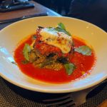 Baked tomato and cheese dish served in a vibrant red sauce on a white plate.