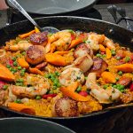 Seafood paella in a black skillet, featuring shrimp, sausage, and vegetables.