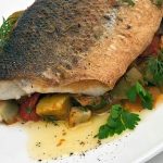 Roasted whole fish fillet served over a bed of roasted vegetables and herbs.
