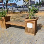 Wooden park bench with planter box in a paved urban plaza with autumn leaves.