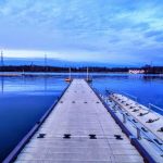 Wooden pier extending over calm blue water under a vast, cloudy sky at dusk.