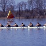 Rowing team on a lake with a colorful triangular flag in the background.