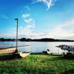 Sunset over a calm lake with boats docked and tall lamppost in the foreground.