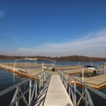 Pier extending over calm water under a bright blue sky with distant tree lines.