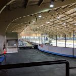 Indoor ice rink with a large, arched ceiling and hockey boards.