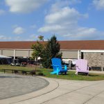 Outdoor market area with white tents, brick building, and people gathering under a blue sky.