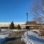 Winter scene with snow-dusted path, modern building, and bare trees under a clear blue sky.
