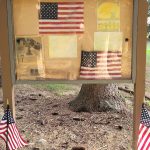 Display board with American flag and historical images mounted on a wooden stand outdoors.