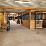 Wooden covered walkway with stalls, showing a rustic agricultural or market setting.