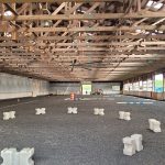 Exposed wooden truss ceiling over a large, dark gravel indoor space with white blocks.