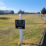 Golf course sign directing to West Course #10 and West Course #1 under a clear blue sky.