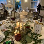 Elegant table setting with tall candleholders, greenery, and a "Table 9" sign at an event.