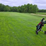 Golf cart with golf bag on a lush green fairway under an overcast sky.
