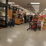 Interior view of a brightly lit grocery store aisle with shoppers and carts.