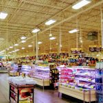 Brightly lit supermarket aisle stocked with various groceries and refrigerated displays.