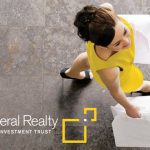 Woman in yellow top stretches on gray floor, holding white bags. Federal Realty logo visible.