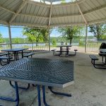 Covered pavilion overlooking a lake with picnic tables and benches.