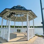 White gazebo overlooking a calm lake under a clear blue sky.