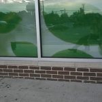 Reflective glass windows showing an outdoor green landscape and interior lighting.