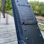 Close-up of a riveted, black iron bridge support beam with "Built by New Jersey Steel & Iron Company 1888" plaque.