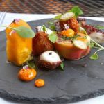 Gourmet appetizer plating on a dark slate board with roasted vegetables and small bites.