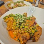 Fried chicken dish topped with herbs and chopped vegetables on a white plate.