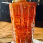 Orange, textured cocktail in a tall glass with a lime garnish on a wooden surface.