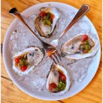 Oysters on ice with tomato and green relish, served on a white plate.