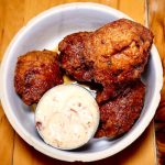 Fried chicken pieces served in a white bowl with dipping sauce on a wooden table.
