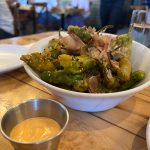 Bowl of seasoned, fried green beans and onions on a wooden table with dipping sauce.