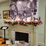 Large black and white historical print above a fireplace mantel with holiday garland.