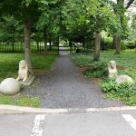 Stone statues flank a gravel path leading through a lush, green park.