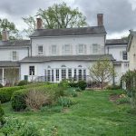 Historic white farmhouse with a porch and green lawn under an overcast sky.