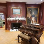 Ornate dark wood piano in a richly decorated room with a fireplace and portrait.