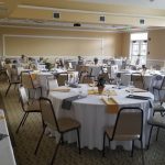 Elegant banquet hall set with round tables, white linens, and floral centerpieces for an event.