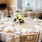 Elegant wedding reception table setting with floral centerpiece and gold chairs.