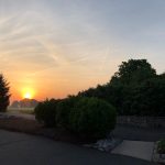 Sunset over a park with trees lining the horizon under a bright, colorful sky.