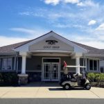 Golf shop building with a golf cart parked in front under a blue, cloudy sky.