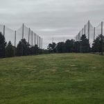 Tennis court surrounded by high netting under an overcast sky with green grass.