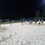 Nighttime beach volleyball game in the sand under stadium lights.