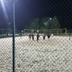 Beach volleyball players on a sand court under nighttime stadium lights.
