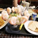 Shrimp cocktail served in a glass bowl on a black tray with crackers and dipping sauce.